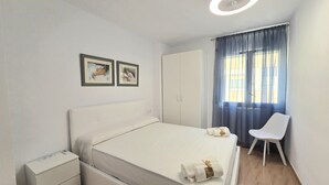 Een slaapkamer met een bed, nachtkastje, stoel, garderobe en twee ingelijste foto’s aan de muur.