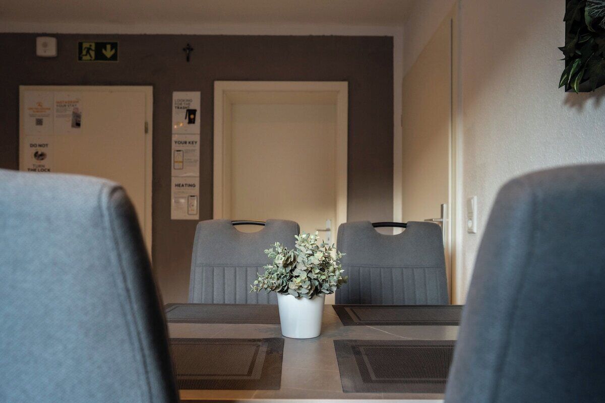 Ein Hotelzimmer mit Esstisch, zwei grauen Stühlen, einer Zimmerpflanze und einer Tür mit einem Schild.