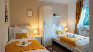 A hotel room with two beds, a wardrobe, a small shelf, and a window with curtains. - Shaft by Loftigo | Apartment with a wellness shower (Übach-Palenberg)