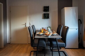 Un comedor con una mesa preparada para dos, sillas, un refrigerador y una puerta.