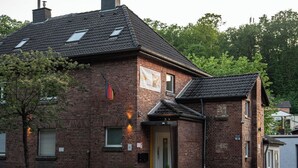 A two-story brick building with a gabled roof, a front entrance, and a small porch area. - Shaft by Loftigo | Apartment with a wellness shower (Übach-Palenberg)