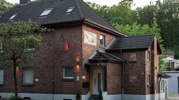Ein zweistöckiges Backsteingebäude mit Satteldach, Hauseingang und einer kleinen Veranda.