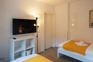 Habitación de hotel con una cama, un televisor sobre un soporte, una mesita de noche y una lámpara.
