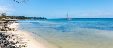 A beach with clear water, a boat, and rocky shoreline.