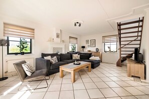 Uma sala de estar com um sofá, uma mesa de centro, um rack para TV e uma escada.