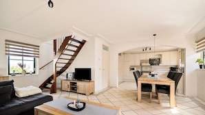 Ein modernes Wohnzimmer mit Sofa, Couchtisch, Fernseher und einer Treppe, die in eine Küche mit Essbereich führt.