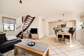 Uma sala de estar moderna com sofá, mesa de centro, TV e escada que leva a uma cozinha com área de jantar.