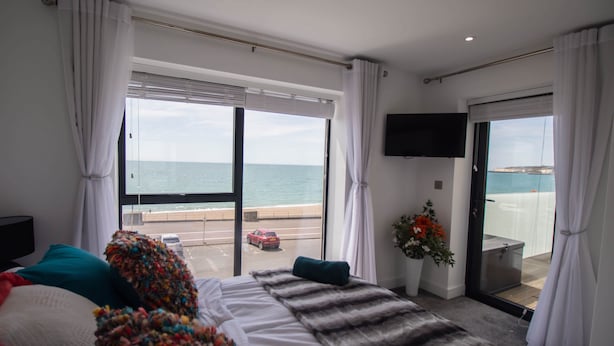 Ett hotellrum med en säng, en TV, en balkong med utsikt över havet och en skjutdörr.