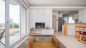 A modern living room with a TV, a glass coffee table, and a kitchen area in the background. - Corporate Stays Edificio Pilar - N4A1 (Asunción)