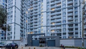 Un edificio residencial de varios pisos con balcones, entrada porticada y vehículos estacionados.