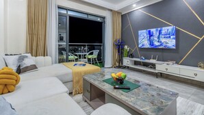 Una sala moderna con sofá, una mesa de centro con fruta, televisor y balcón con vistas.