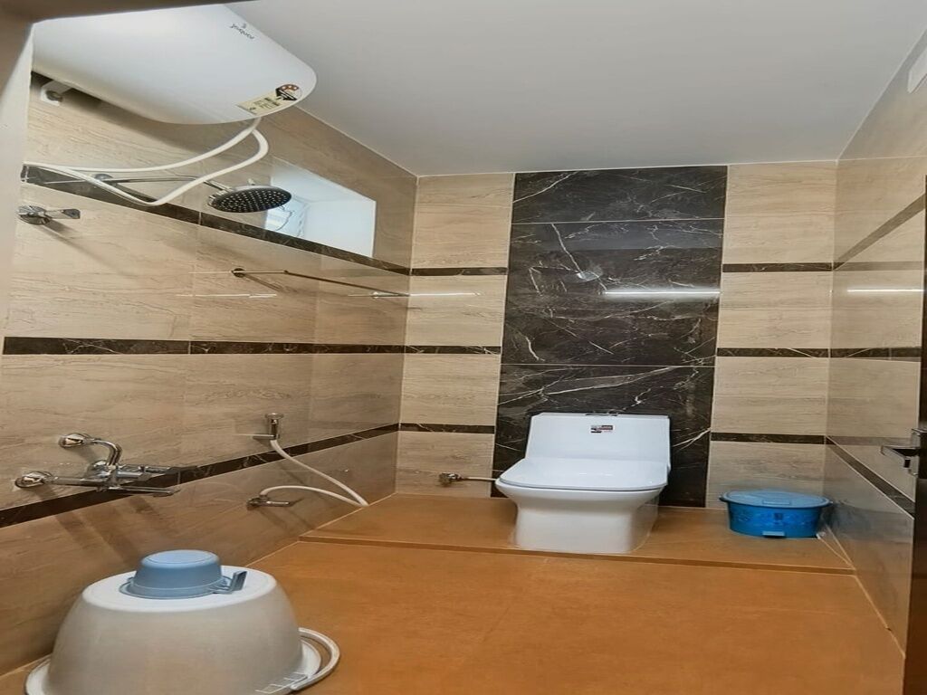 Un baño con inodoro, ducha y secador de pelo sobre una estantería.