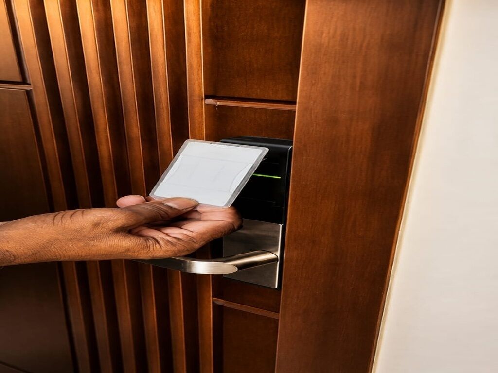 A hand holding a card near a metallic door handle, likely for a keycard or access device.