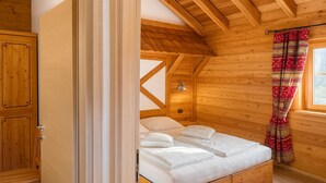 Een slaapkamer in een houten chalet, met een bed, een bankje en een raam met gordijnen.
