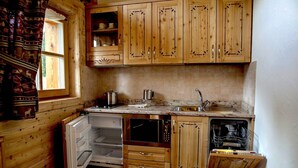 Een kleine keuken met houten kastjes, een inbouwvaatwasser en een raam met gordijnen.