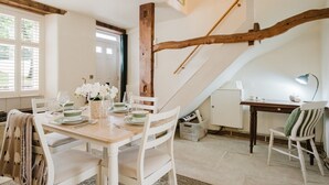 Ein Essbereich mit einer Holztreppe, weißen Stühlen, einem gedeckten Holztisch für vier Personen und einem Schreibtisch mit Lampe.