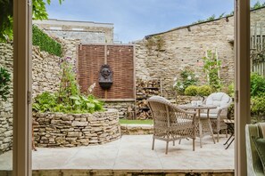 A stone-walled patio with wicker furniture and a decorative wall-mounted light fixture. - Beautiful Cottage in Centre of Cirencester (Cirencester)