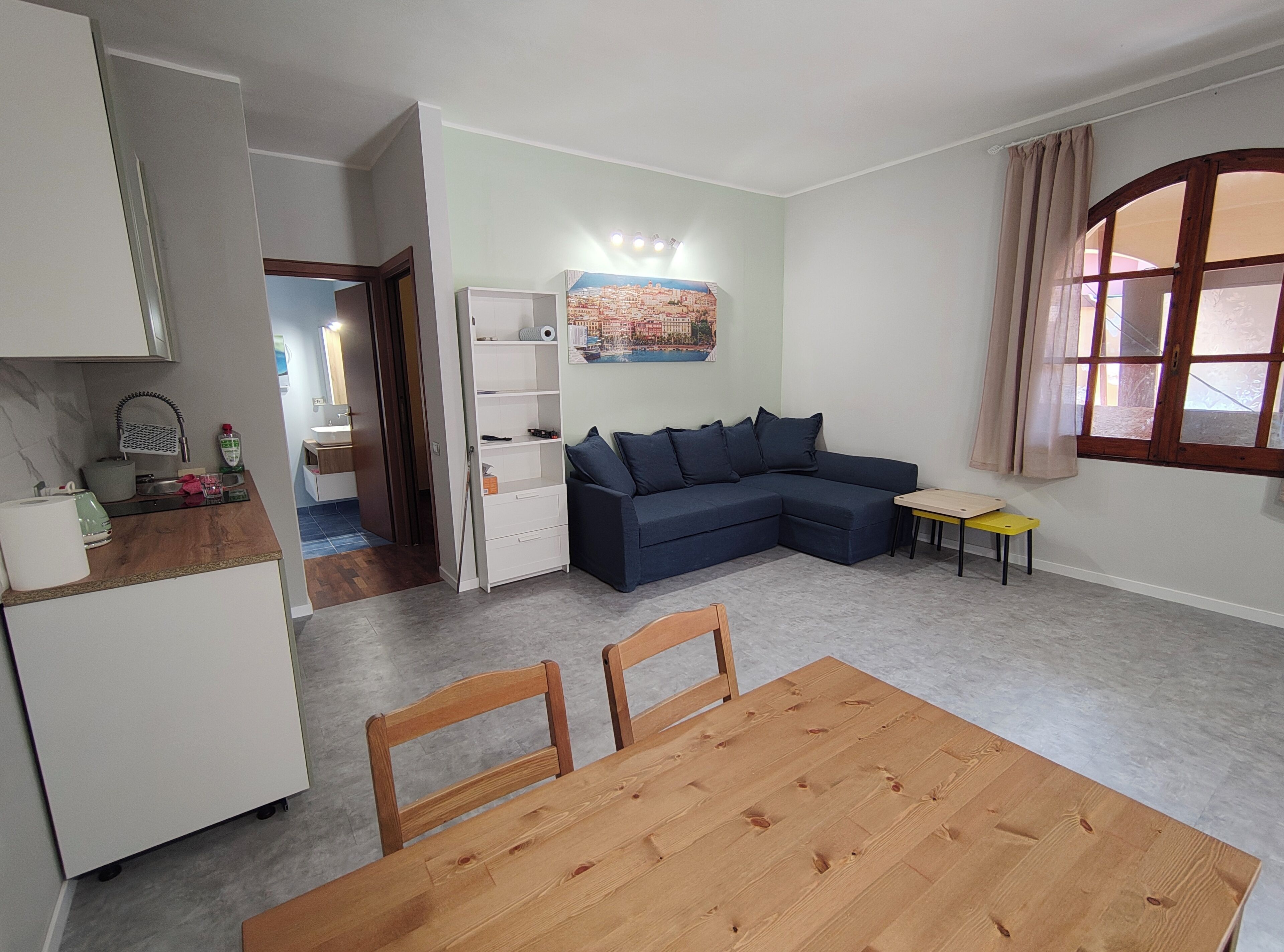 Una sala de estar con sofá, una mesa de comedor con sillas, una zona de cocina y un ventanal con cortinas.