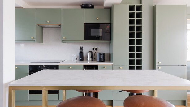 Une cuisine moderne dotée d’un îlot central, d’appareils électroménagers intégrés et d’un coin repas avec des tabourets.