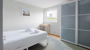 Une chambre à coucher avec un lit, une petite table, une fenêtre donnant sur un beau paysage et une armoire.