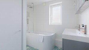 A modern bathroom with a freestanding bathtub, a window, and a sink with a soap dispenser. - Refined 3BDR Retreat with Skyline Views (Greater London)