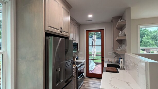 A modern kitchen with stainless steel appliances, a wooden floor, and a view through a glass door to the outdoors.