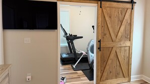 A room with a sliding barn door, a treadmill, a washing machine, and a mounted television.