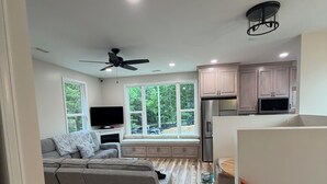 A modern living room with a sofa, a TV, and a kitchen area with cabinets and a microwave.