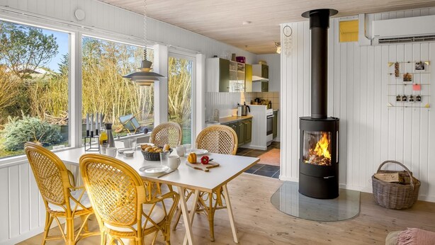 A modern kitchen with a central wood-burning stove, white cabinetry, and a dining area with wicker chairs. - "Ruka" - 600m from the sea by Interhome (Løkken)