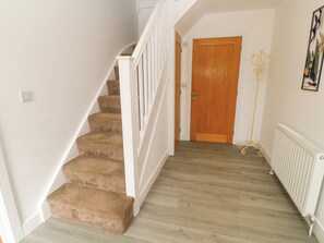 A staircase with carpeted steps, a white railing, a wooden door, and a radiator on the floor. - Rosevale Villa (St Ives)