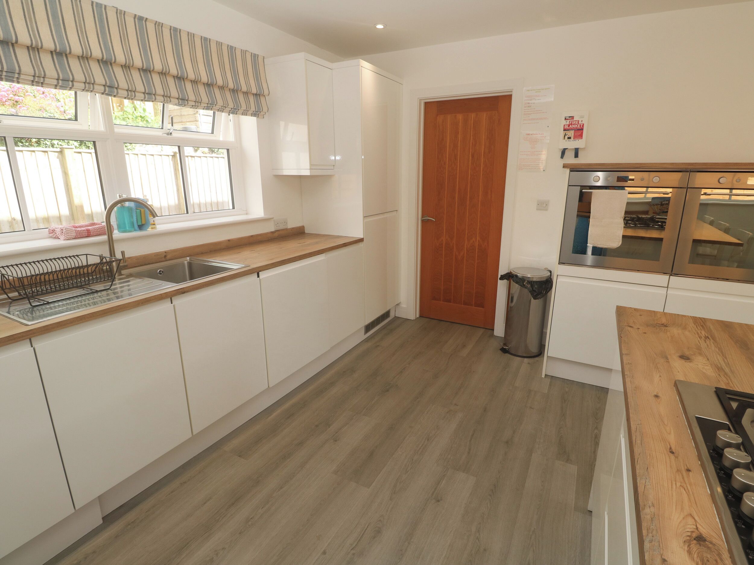 Cocina con armarios blancos, encimera de madera, pileta de acero inoxidable, puerta de madera y campana extractora de acero inoxidable.