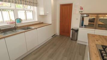 Cocina con armarios blancos, encimera de madera, pileta de acero inoxidable, puerta de madera y campana extractora de acero inoxidable.