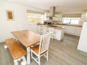 A modern kitchen with a wooden dining table, white chairs, a central island, and a built-in stove. - Rosevale Villa (St Ives)