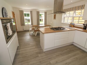 A modern kitchen with a central island, white cabinetry, and a built-in oven. - Rosevale Villa (St Ives)