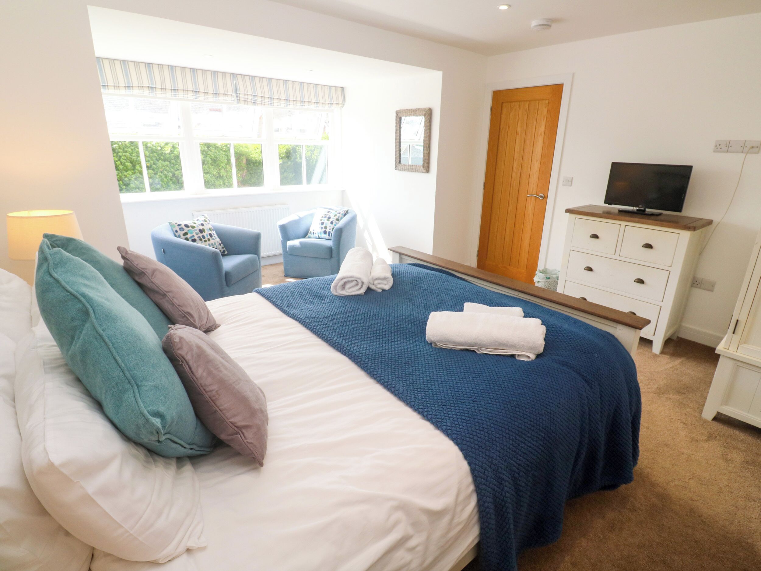 A bedroom with a bed, two chairs, a TV, and a wardrobe.