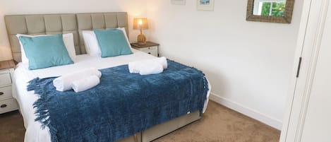 A neatly made bed with a blue blanket and white towels, a bedside lamp, and framed pictures on the wall.