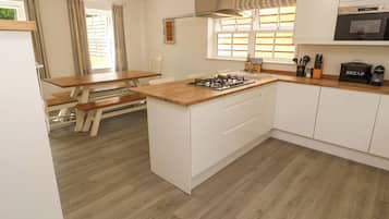 A modern kitchen with a wooden island, white cabinetry, a gas stove, and a microwave.