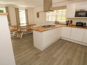 A modern kitchen with a wooden island, white cabinetry, a gas stove, and a microwave. - Rosevale Villa (St Ives)