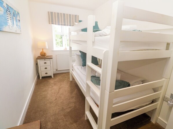 A bunk bed room with a nightstand, lamp, window with curtains, and a radiator. - Rosevale Villa (St Ives)