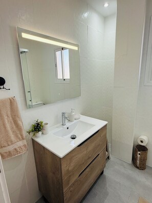 Een badkamer met een witte wastafel, houten wastafelmeubel, een spiegel met verlichting en een handdoekrek.