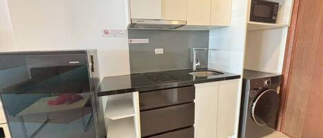 Una cocina compacta con microondas integrado, lavadora y refrigerador pequeño.