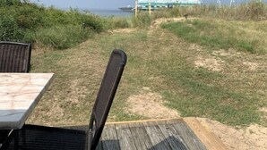 Une terrasse avec une table et des chaises, un espace gazonné menant à un bâtiment, et une vue sur la mer.