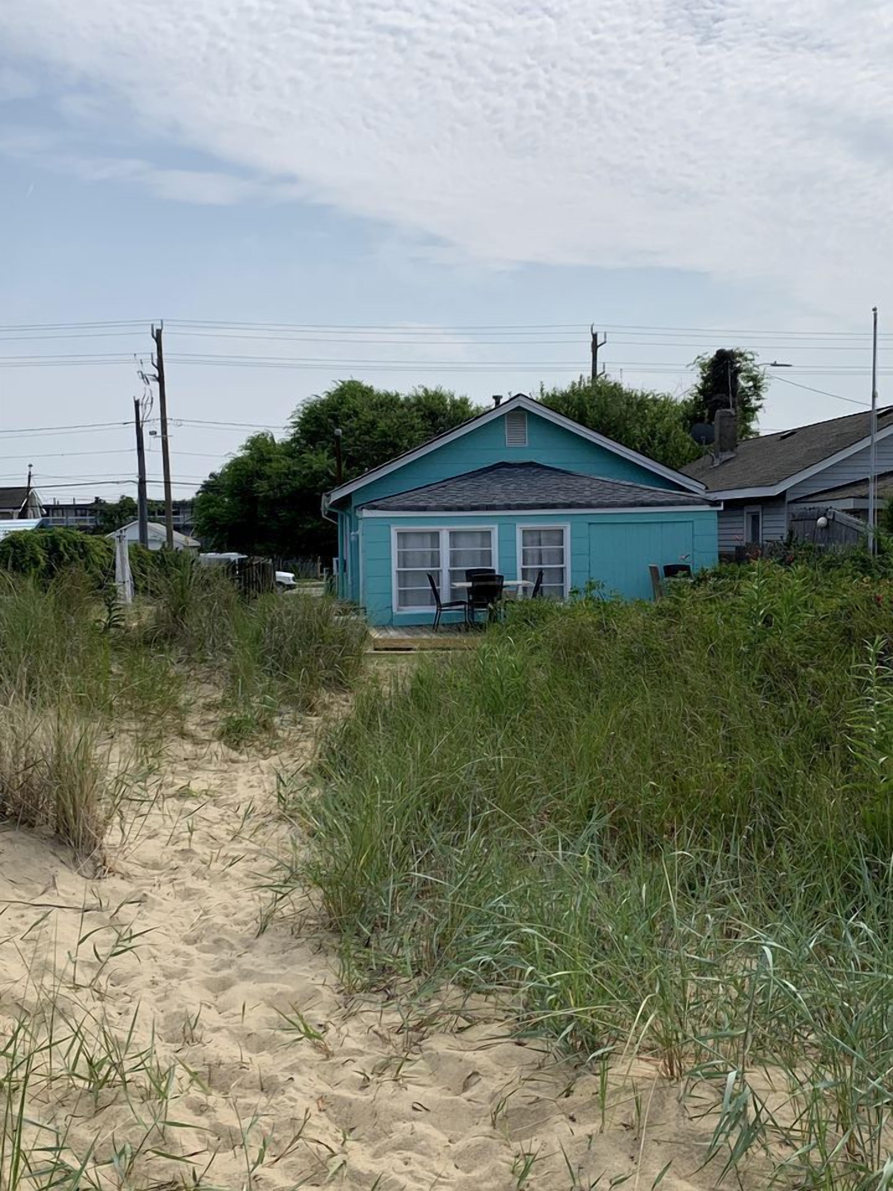 A house with a sandy path leading to it, surrounded by tall grass.