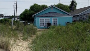 Une maison avec un chemin de sable menant à l’entrée, entourée d’herbes hautes.