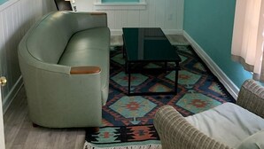 Une pièce aux murs de couleur turquoise, avec un fauteuil aux lignes arrondies, une petite table et un tapis à motifs.