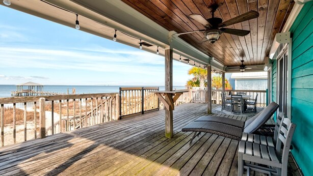 A wooden deck with a ceiling fan, outdoor seating, and a view of the beach and ocean. - Pet-Friendly Cottage with Private Beach Access & Pier in Dauphin Island, Alabama (Dauphin Island)