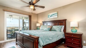 A bedroom with a bed, a ceiling fan, a nightstand, a lamp, a dresser, and a view through a glass door. - Pet-Friendly Cottage with Private Beach Access & Pier in Dauphin Island, Alabama (Dauphin Island)
