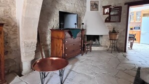 Una stanza con pareti in pietra, un camino, un comò di legno, una televisione e un tavolo.