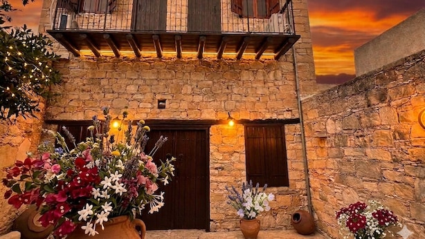 Un edificio in pietra con un balcone, due porte e vasi di fiori.
