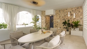 A dining area with a round table, wicker chairs, potted plants, and a stone wall. - Nama Summer Retreat Mikra Mantinia Beachfront Gem (Kalamata)